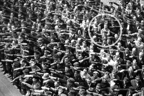 这张照摄于1936年，记录了汉堡一家船厂为纳粹海军训练船Horst Wessel号建成出航时举行的一次大型集会。人群后面有一个人双手交叉在胸前，明显与众不同。