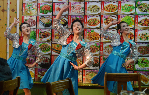 2013年2月11日，朝鲜女服务员们在中国边境城市丹东的一家朝鲜国营餐厅里大菜单屏幕前面为顾客们表演舞蹈。