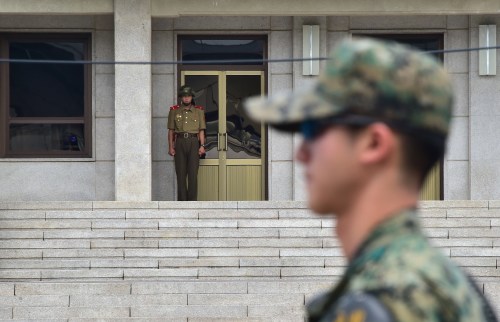 2015年7月22日，一名韩国士兵（右）在站岗，一名朝鲜士兵（中）在面向朝韩非军事区中的板门店停战村。