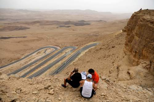 2018年5月6日，内盖夫沙漠的以色列南部城市Mitzpe Ramon附近，人们坐在悬崖上，俯瞰着Machtesh Ramon的火山口。以色列正在寻求开放内盖夫沙漠地区的旅游业。