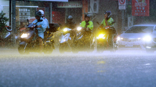 臺北街頭機車騎士全副武裝在雨中等待交通燈轉綠。