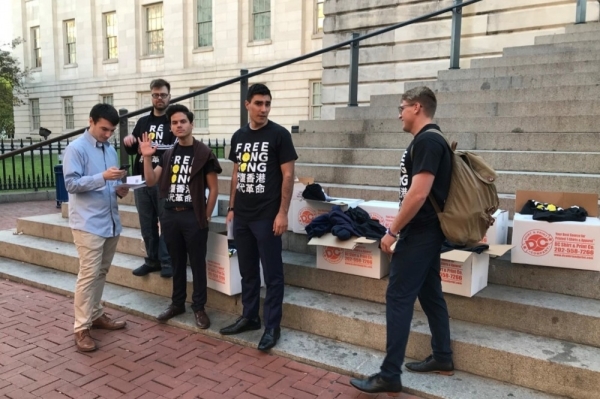 四位白人面孔的美國人穿著「FREE HONG KONG」、「光復香港，時代革命」的T恤，並擺放著十箱裝著各種尺寸，寫著同樣字樣的T恤給往來的行人。（圖片由作者提供）