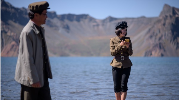 图为一名朝鲜学生拿着手机，站在长白山天池旁