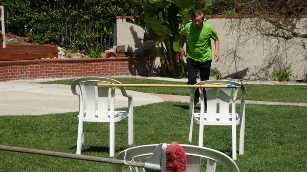 外号“火箭阿公”的77岁常青组田径选手许永忠在自家后院用扫把、椅子搭起的栏架，作为训练跨栏的器材。