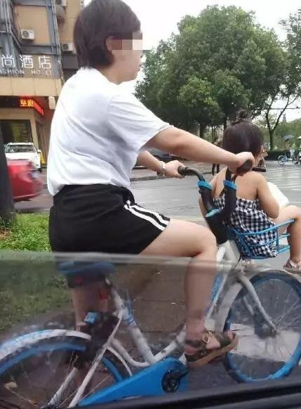 大陆女子骑着共用自行车，车筐放小孩。