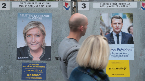 2017年法国总统大选变数最多，4月19日，两名选民经过投票站，正在看墙上贴的竞选海报 