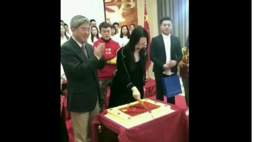 在中國駐保加利亞大使張海舟身旁的女子，她手持長刀，從中間切開有五星紅旗圖案的蛋糕，此時張海舟也微笑鼓掌