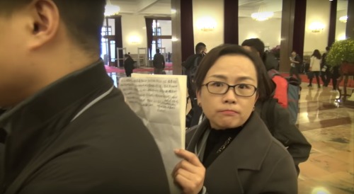 一位女士躲在記者身後，拿著受訪人大代表的稿子