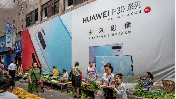 2019年6月1日，中國西南部雲南省芒市，一名女子在中國華為的廣告牌前與女兒一起購物。