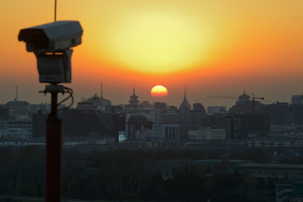The sun sets behind the Beijing skyline and a security camera,）
